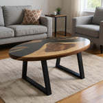 Măsuță de cafea unică. Blat oval din nuc masiv și rășină epoxidică neagră, așezată elegant într-un living modern. Blatul de tip River Table se completează armonios cu o canapea confortabilă și un covor texturat, creând un punct focal sofisticat și o atmosferă primitoare.